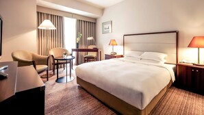 Habitación de hotel con una cama grande, dos sillas, un escritorio, una lámpara y una mesita de noche.