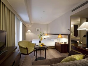 Une chambre d’hôtel comprenant un lit, un bureau, une chaise, un canapé, une table de chevet avec une lampe, une horloge et un miroir.