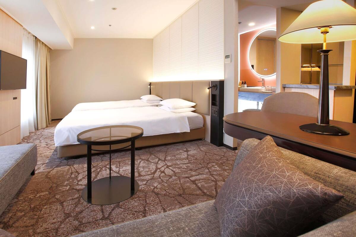 Ein Hotelzimmer mit Bett, einem kleinen Tisch, einer Couch und einer Lampe.