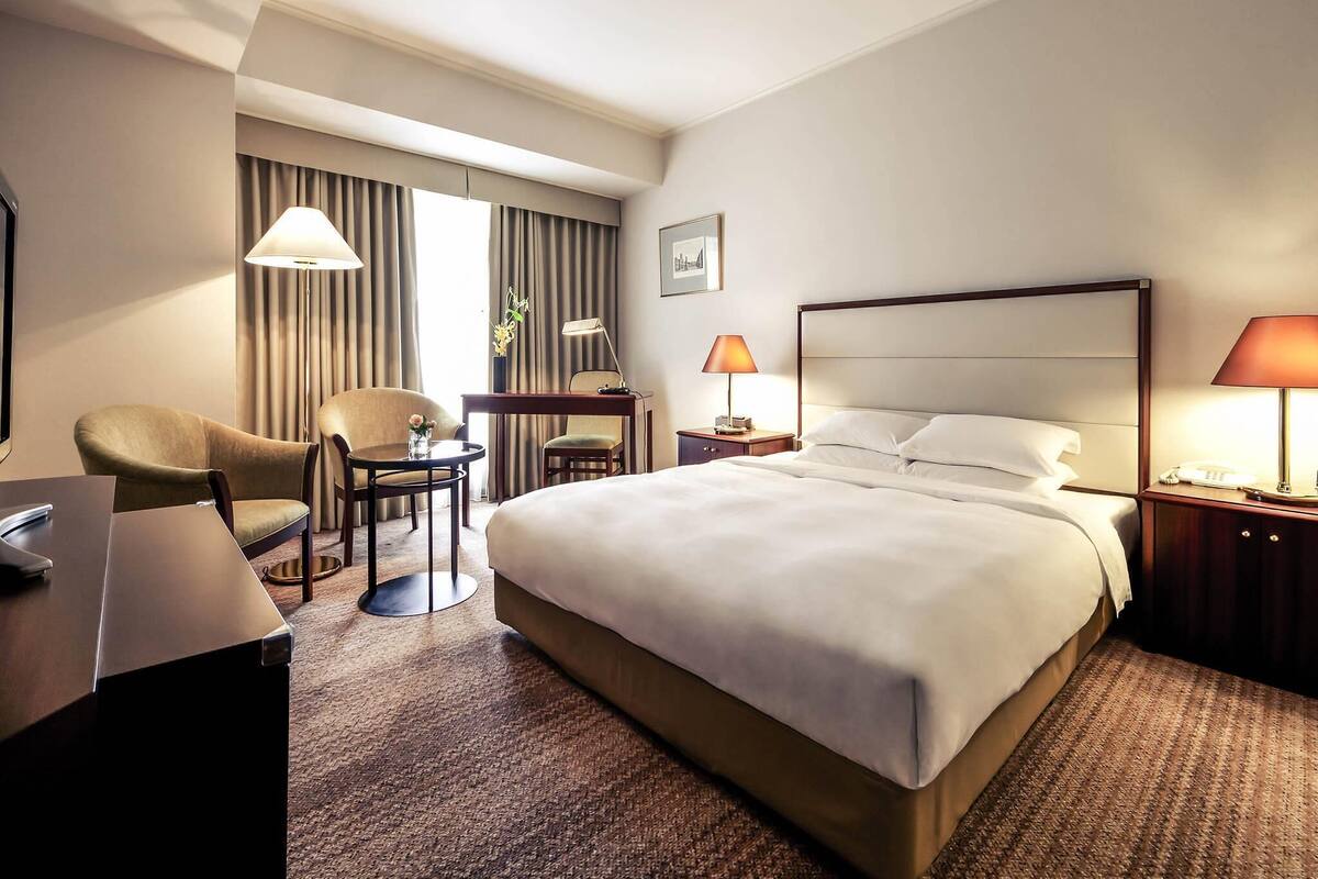 Ein Hotelzimmer mit einem großen Bett, zwei Stühlen, einem Schreibtisch, einer Lampe und einem Telefon.
