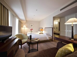 Ein Hotelzimmer mit Bett, Fernseher, Schreibtisch, Stuhl, Lampe und Spiegel.
