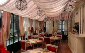 A dining area with tables set for service, draped curtains, and hanging crystal chandeliers.