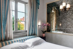 A bedroom with a bed, curtains, a potted plant, a window, and a mirror.