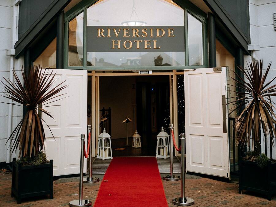 The Riverside Hotel entrance with a red carpet, white doors, and potted plants.