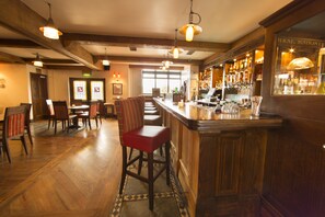Una zona de bar con mobiliario de madera, una barra y luces colgantes.
