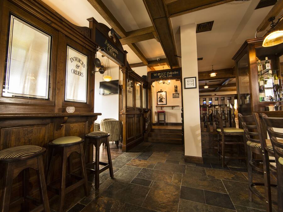 A bar area with wooden bar stools, a stone floor, and a sign for 'Accounts Office'.