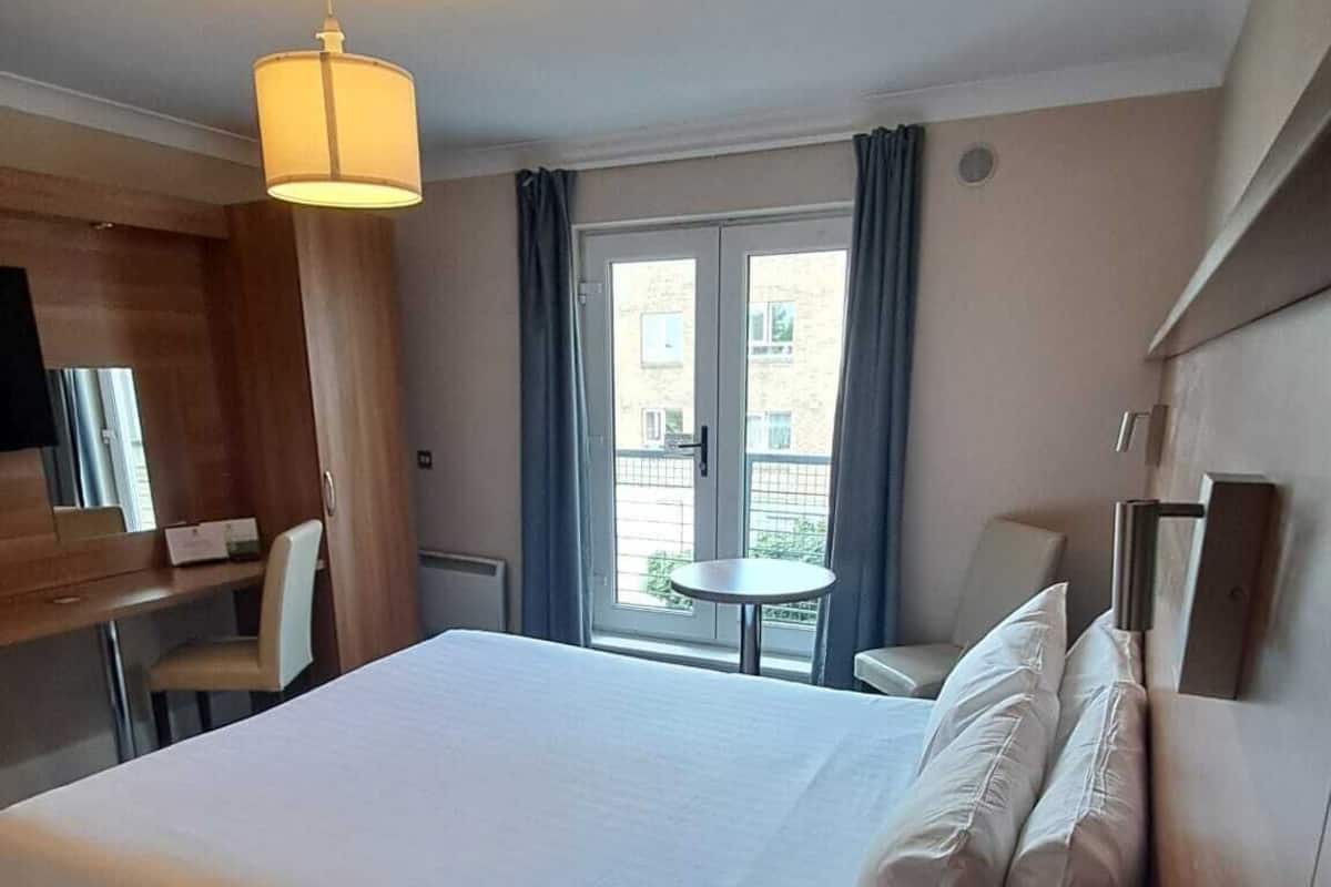 Habitación de hotel con una cama grande, un escritorio, una silla, una mesita, un teléfono y una ventana con cortinas.