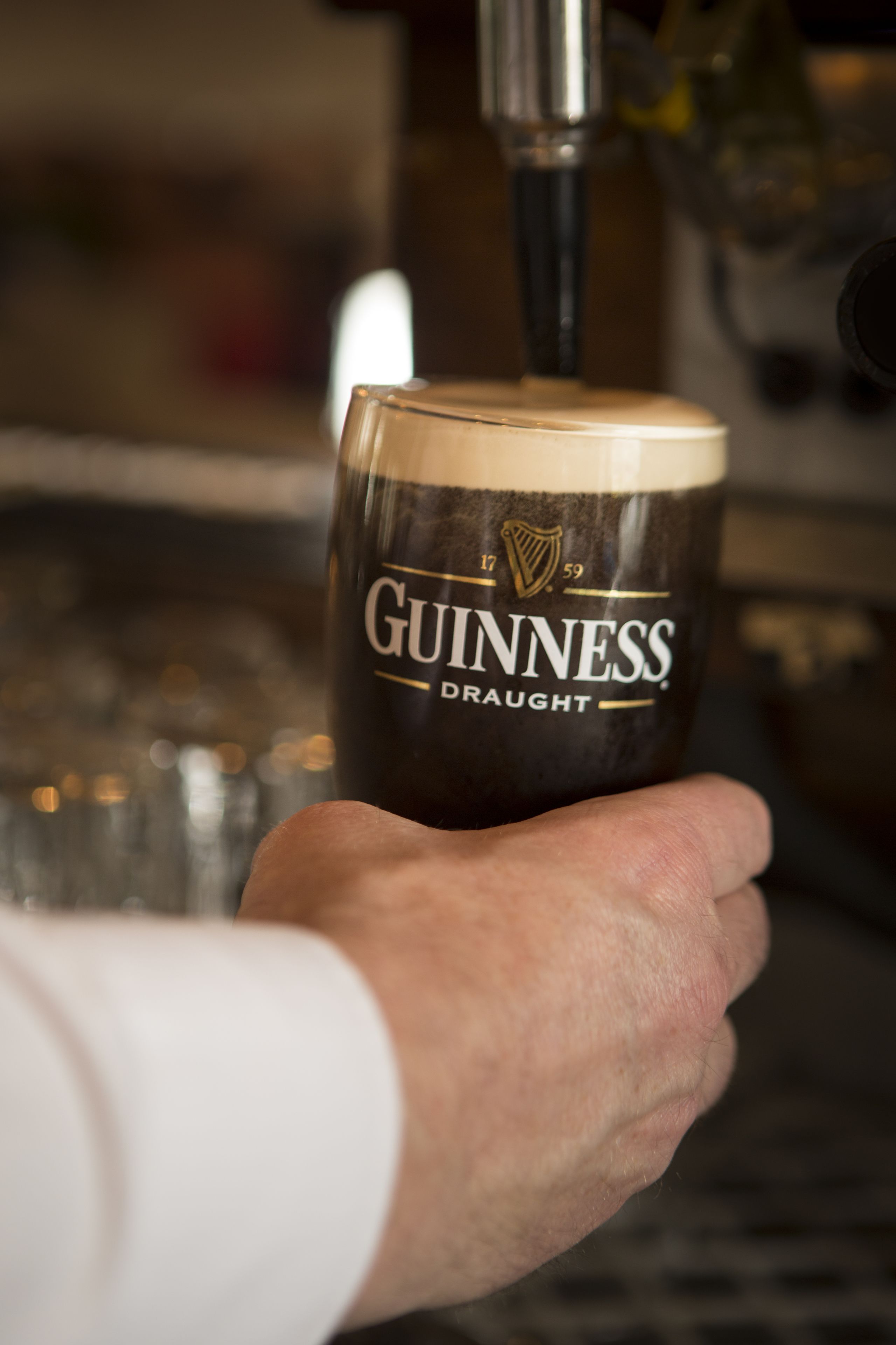 A hand holding a Guinness branded glass mug.