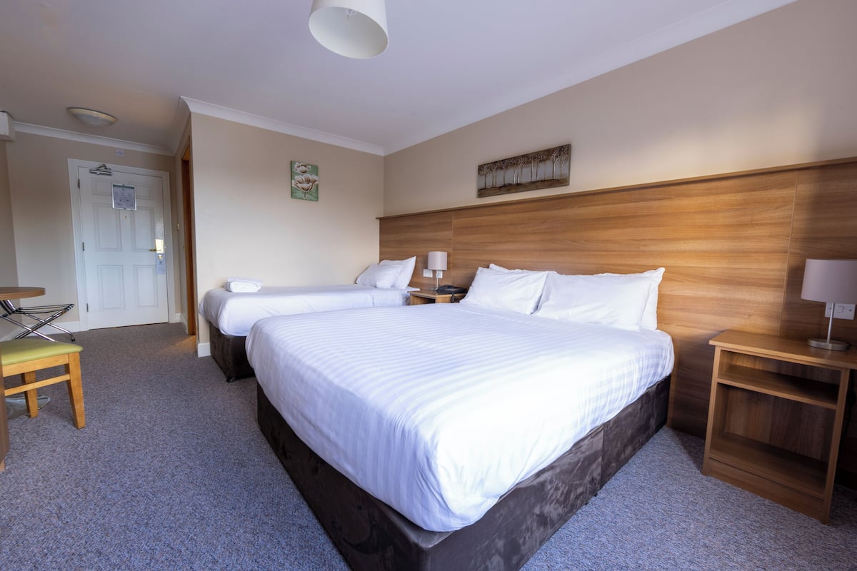 Habitación de hotel con dos camas, cabecero de madera, una mesita y una silla.
