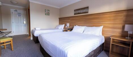 A hotel room with two beds, a wooden headboard, a small table, and a chair.
