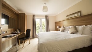 Una habitación de hotel con una cama grande, un escritorio con una silla, una televisión y una ventana con cortinas.