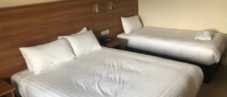 A hotel room with two beds, each with white linens and pillows, a wooden headboard, and a nightstand with a phone.