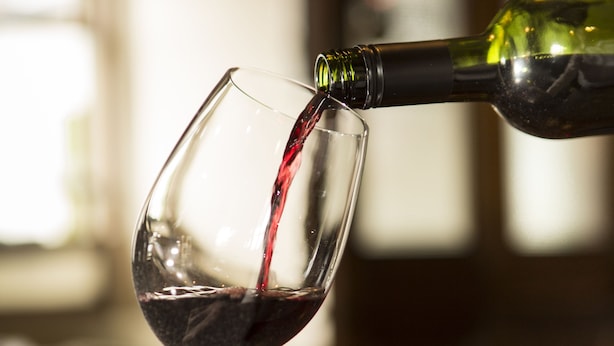 A hand pouring red wine from a green bottle into a clear wine glass. - Riverside Hotel (Sligo)