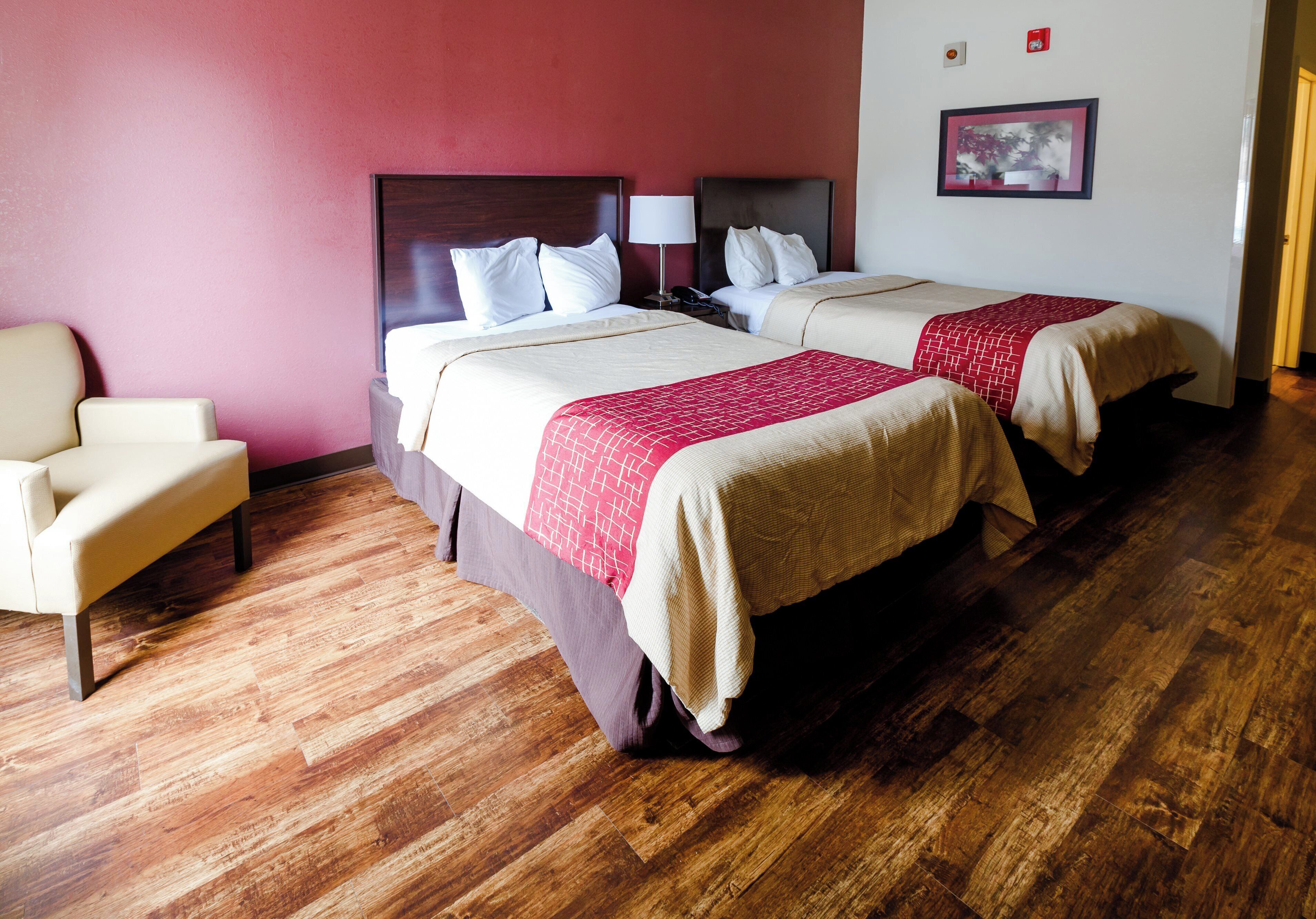 Une chambre d’hôtel avec deux lits, une chaise et un plancher en bois.