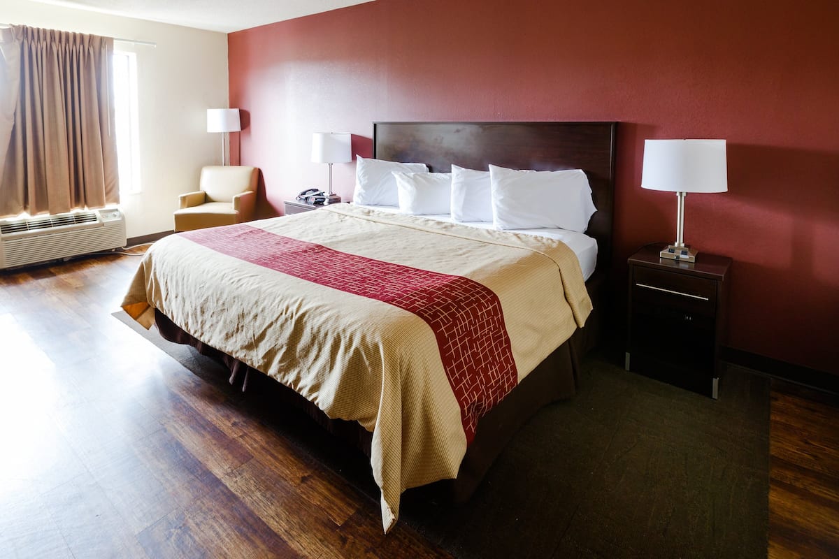 Ein Hotelzimmer mit einem großen Bett, zwei Nachttischlampen, einem Sessel und einem Schreibtisch mit Telefon.