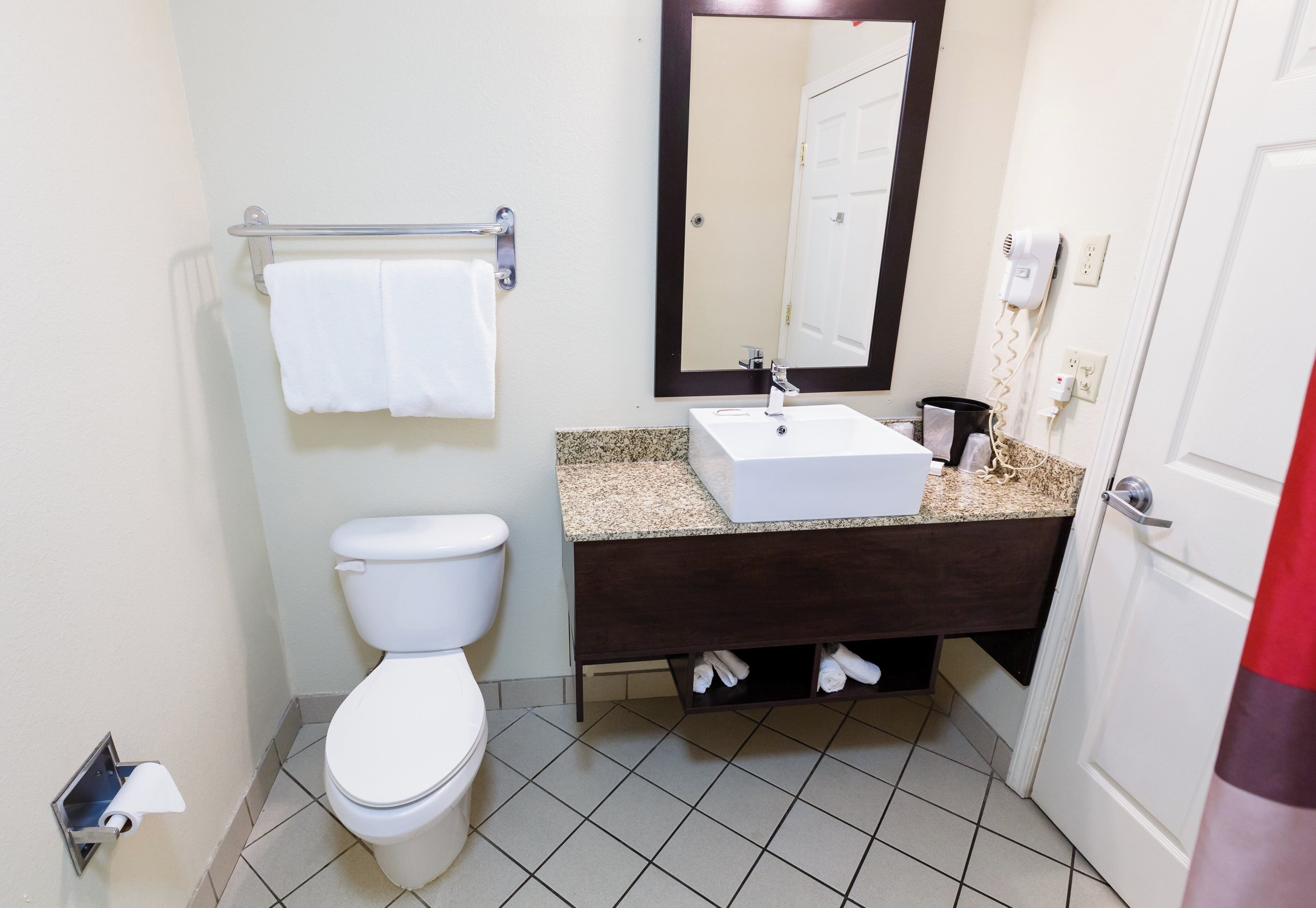 A bathroom with a toilet, sink, mirror, and towel rack.