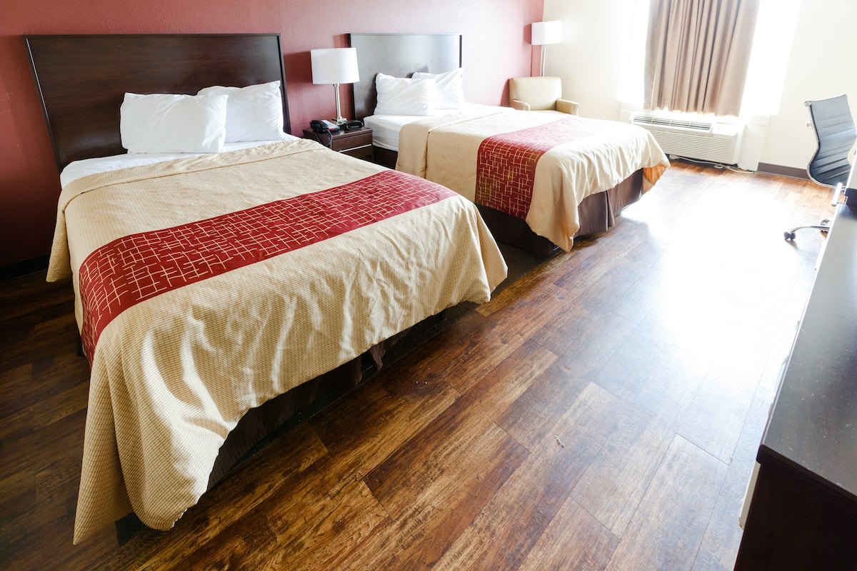 Ein Hotelzimmer mit zwei Betten, einem Schreibtisch, einem Stuhl und einem Fenster mit Vorhängen.