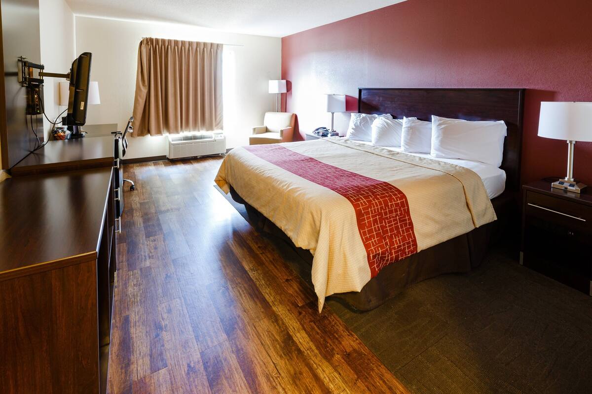 Una habitación de hotel con una cama grande, suelo de madera, un escritorio y una televisión.