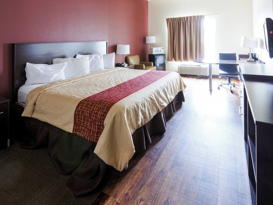 Habitación de hotel con cama, mesitas de noche, escritorio, silla, televisor y ventana con cortinas.