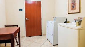 Una pequeña cocina americana con una puerta de madera, una lavadora, una mesa y un cuadro en la pared.