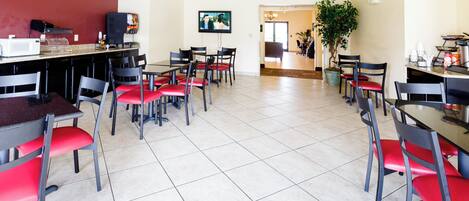 A dining area with multiple tables and chairs, a television mounted on the wall, and a potted plant.