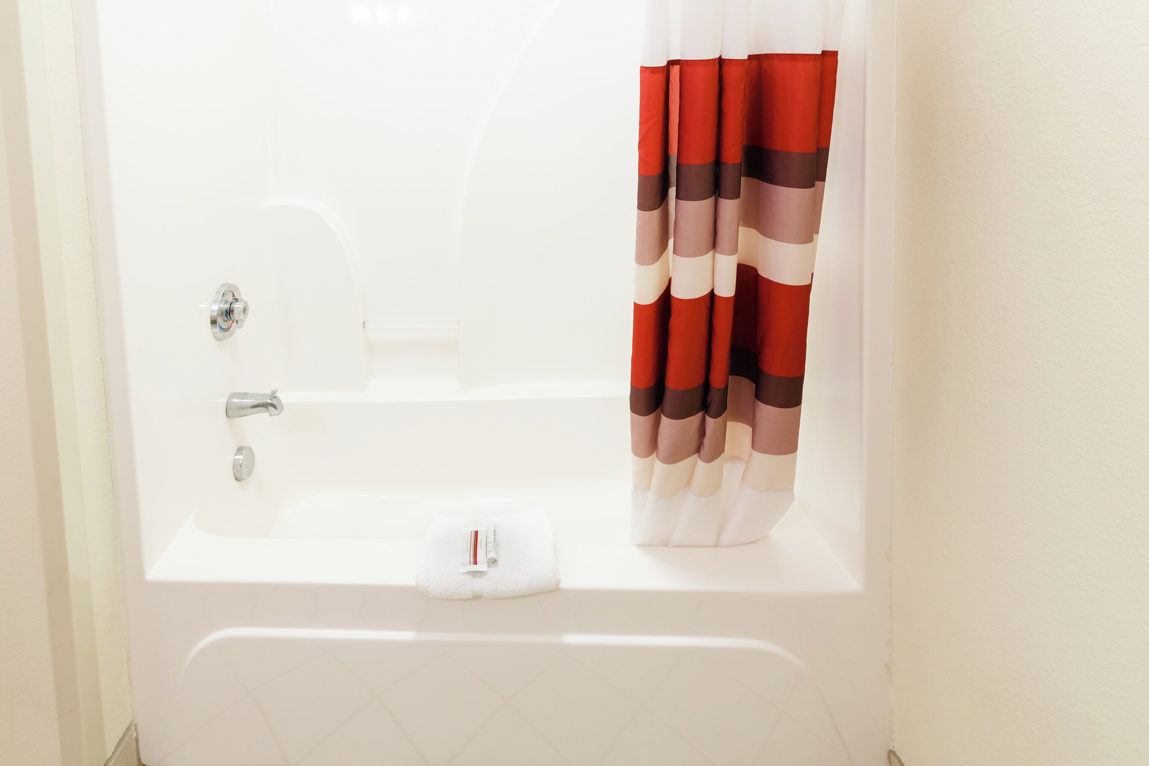 A white bathtub with a shower head, a towel, and a striped shower curtain.