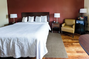 Una habitación de hotel con una cama grande, dos mesitas de noche con lámparas, una silla, un escritorio con teléfono y un refrigerador pequeño.