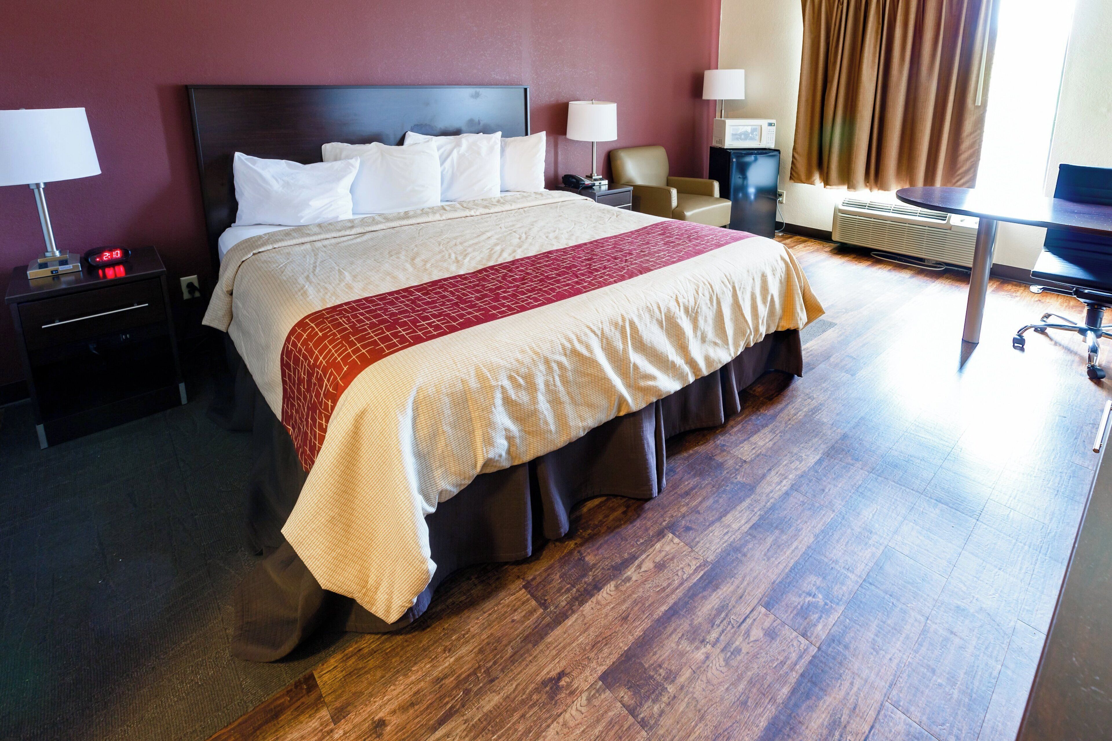 Een hotelkamer met een groot bed, nachtkastjes, een bureau, een stoel en een raam met gordijnen.