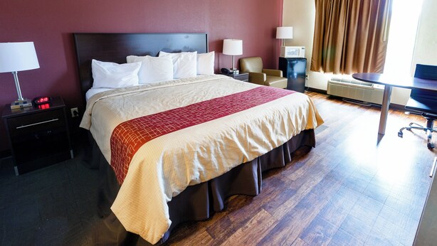 Habitación de hotel con una cama grande, mesitas de noche, un escritorio, una silla y una ventana con cortinas.