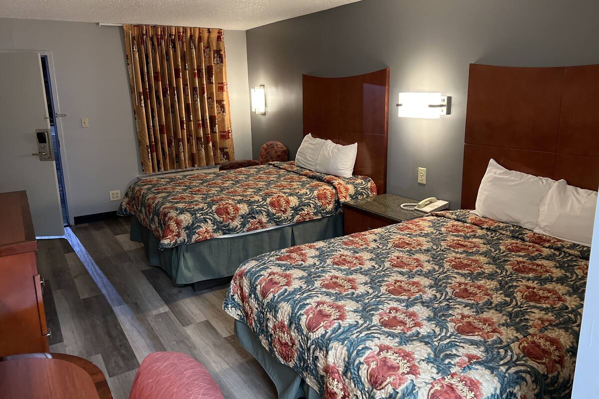Une chambre d’hôtel avec deux lits, une tête de lit en bois, un téléphone et un rideau.