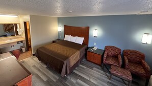 A hotel room with a bed, a desk, a chair, a nightstand, and a mirror.
