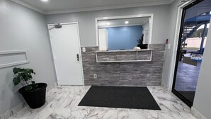 A reception area with a marble floor, a potted plant, a closed door, and a reception desk with a mirror above it.