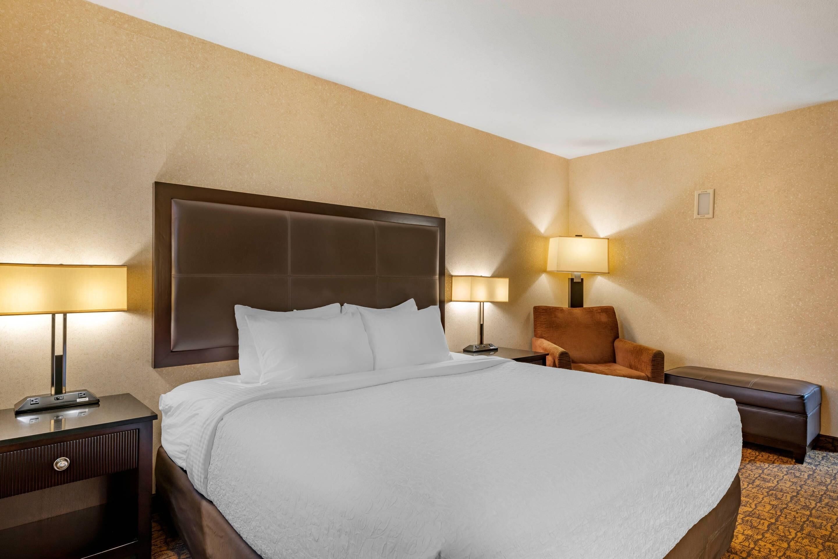 Ein Hotelzimmer mit einem großen Bett, zwei Nachttischlampen, einem Sessel und einem kleinen Tisch.
