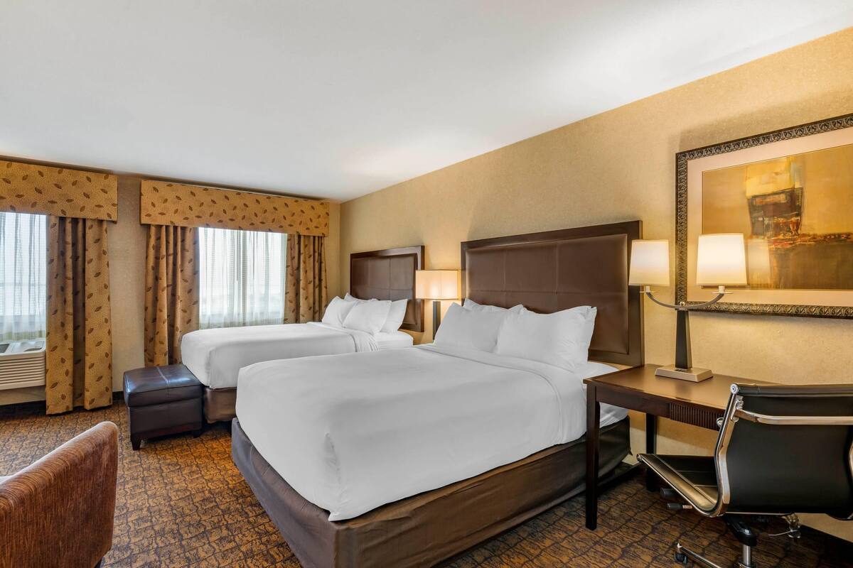 A hotel room with two beds, a desk, a chair, a lamp, and a large mirror on the wall.