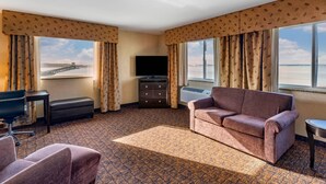 Habitación de hotel con sofá, escritorio, silla, televisión y vista a un puente y al agua.