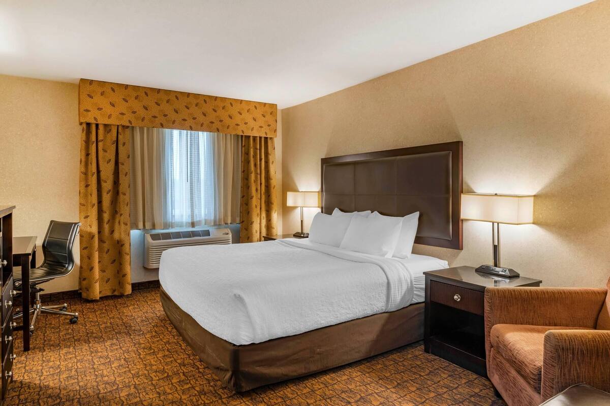 A hotel room with a large bed, two bedside tables with lamps, a desk with a chair, and a window with curtains.