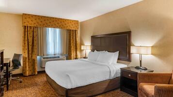 A hotel room with a large bed, two bedside tables with lamps, a desk with a chair, and a window with curtains.