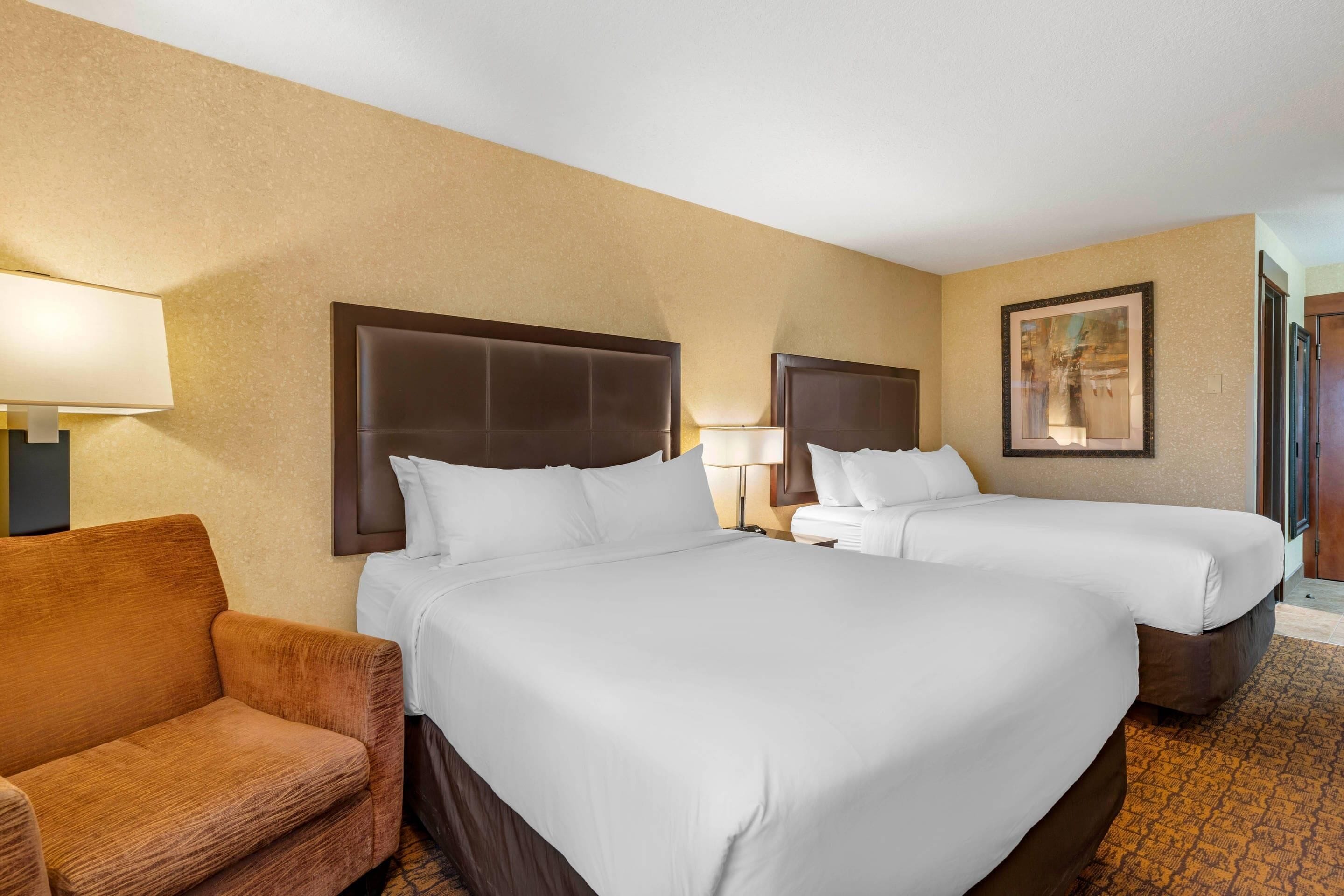 Quarto de hotel com duas camas, um sofá e um quadro na parede.