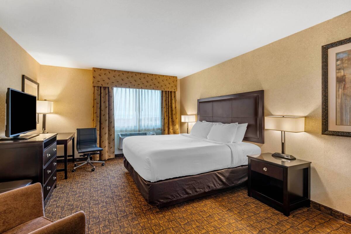 A hotel room with a large bed, a desk with a computer, a TV, and a chair.