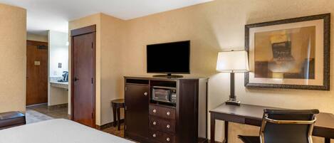 A hotel room with a bed, a desk with a lamp, a television, a minibar, and a chair.