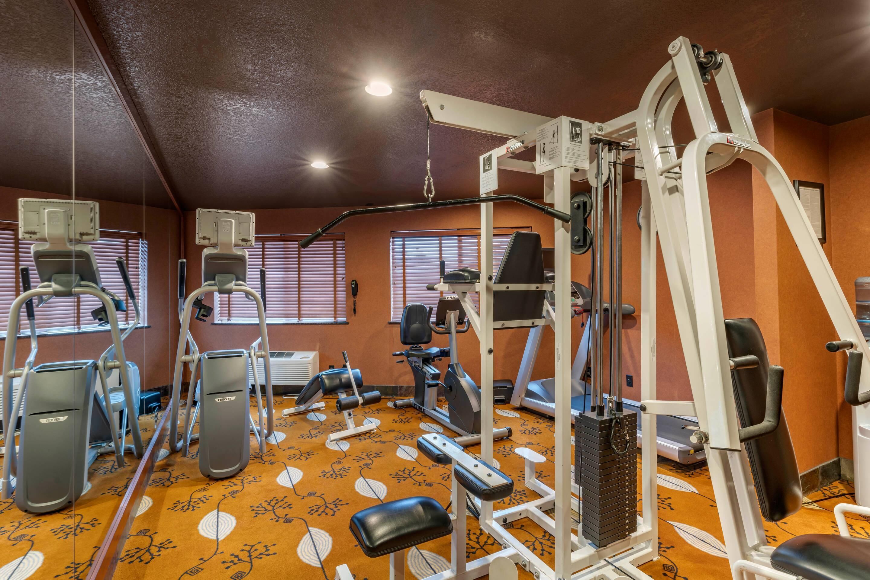 Un gimnasio con varios equipos de ejercicio, incluyendo cintas de correr, elípticas y máquinas de pesas.