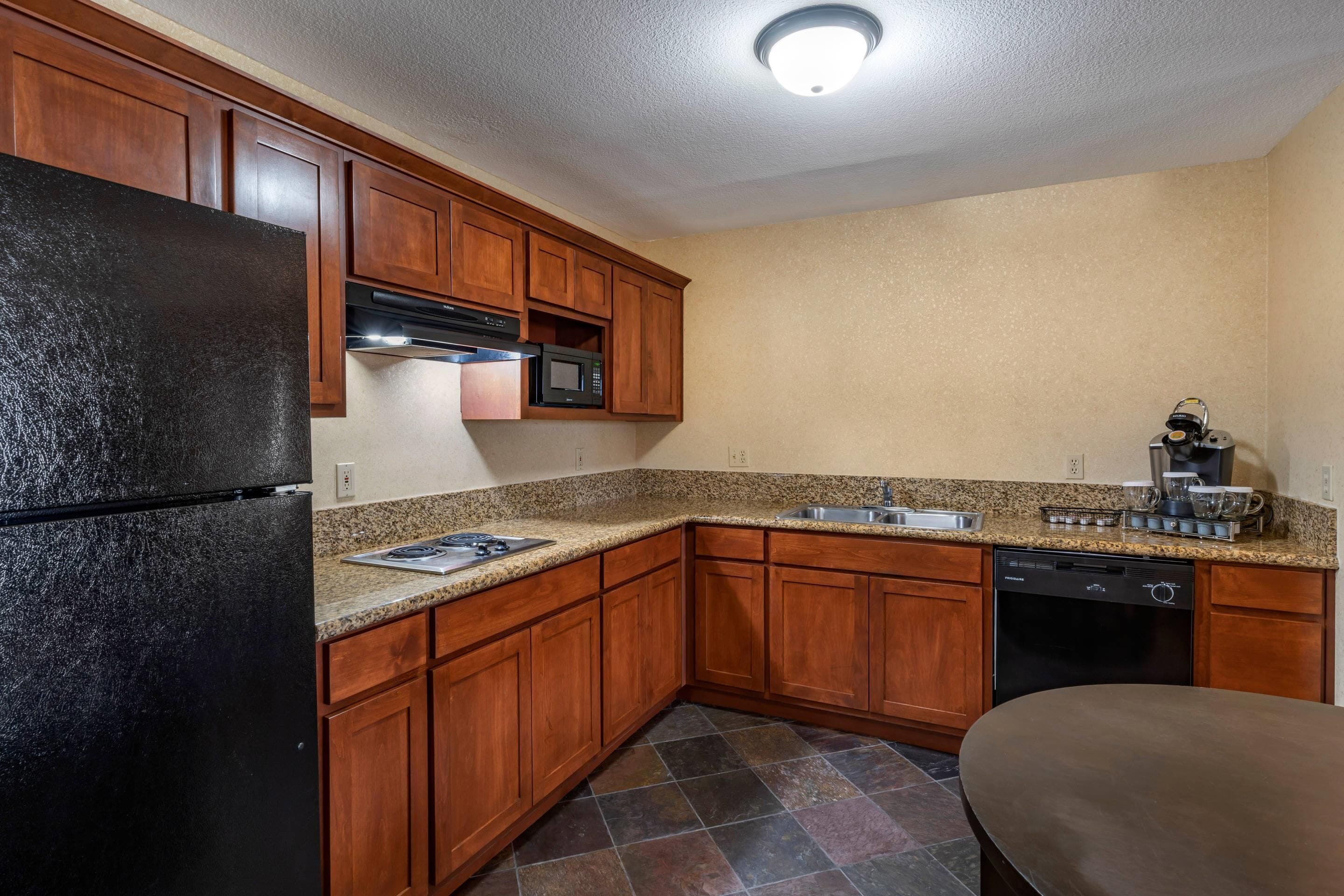 A kitchen with wooden cabinets, a black refrigerator, a microwave, a dishwasher, and a granite countertop.