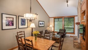 A dining area with a wooden table and chairs, a chandelier, framed artwork on the wall, and a stone fireplace. - First Tracks Lodge, by Lodging Ovations (Whistler)