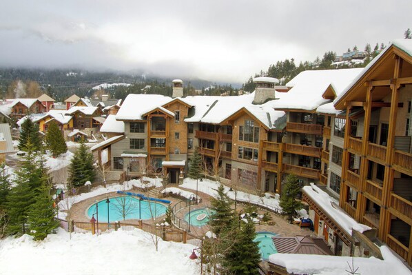A resort with multiple wooden buildings, a central pool area, and snowy surroundings.
