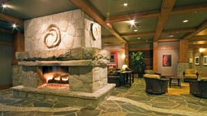 A stone fireplace with a fire, surrounded by wicker furniture and a stone floor. - First Tracks Lodge, by Lodging Ovations (Whistler)
