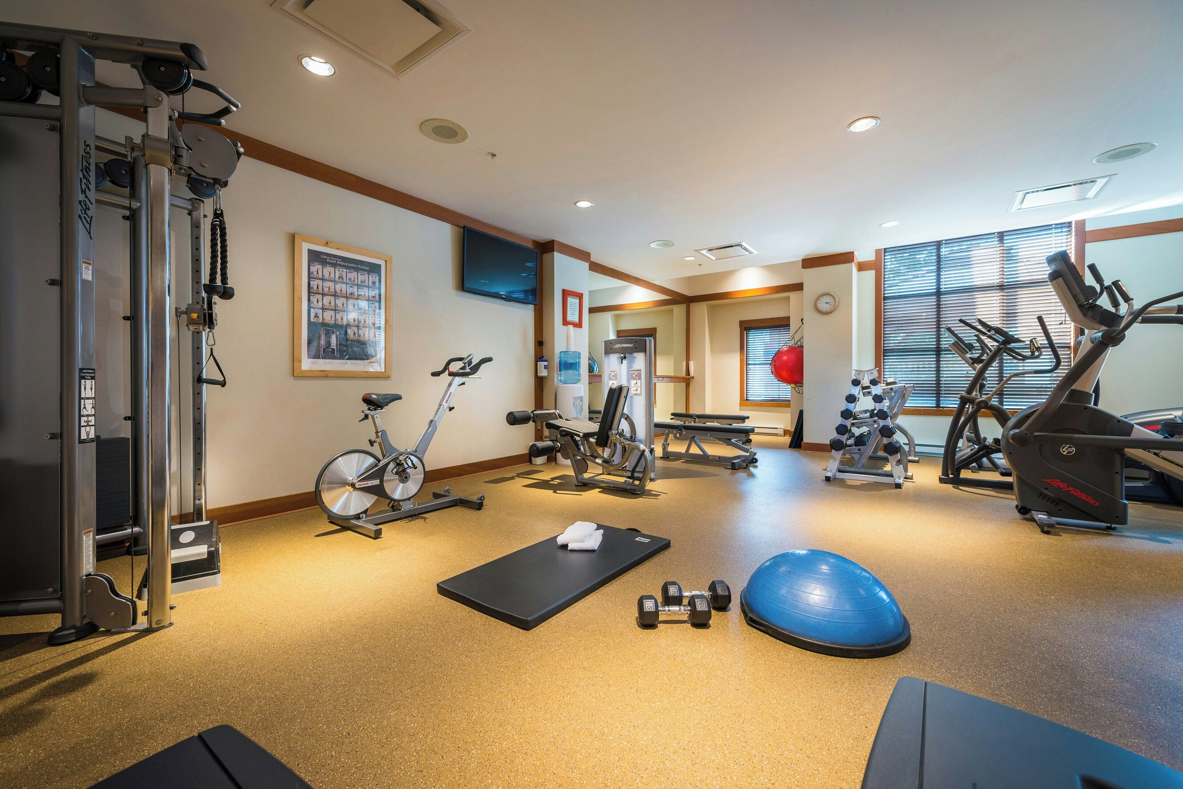 A gym with exercise equipment, a yoga mat, and dumbbells.