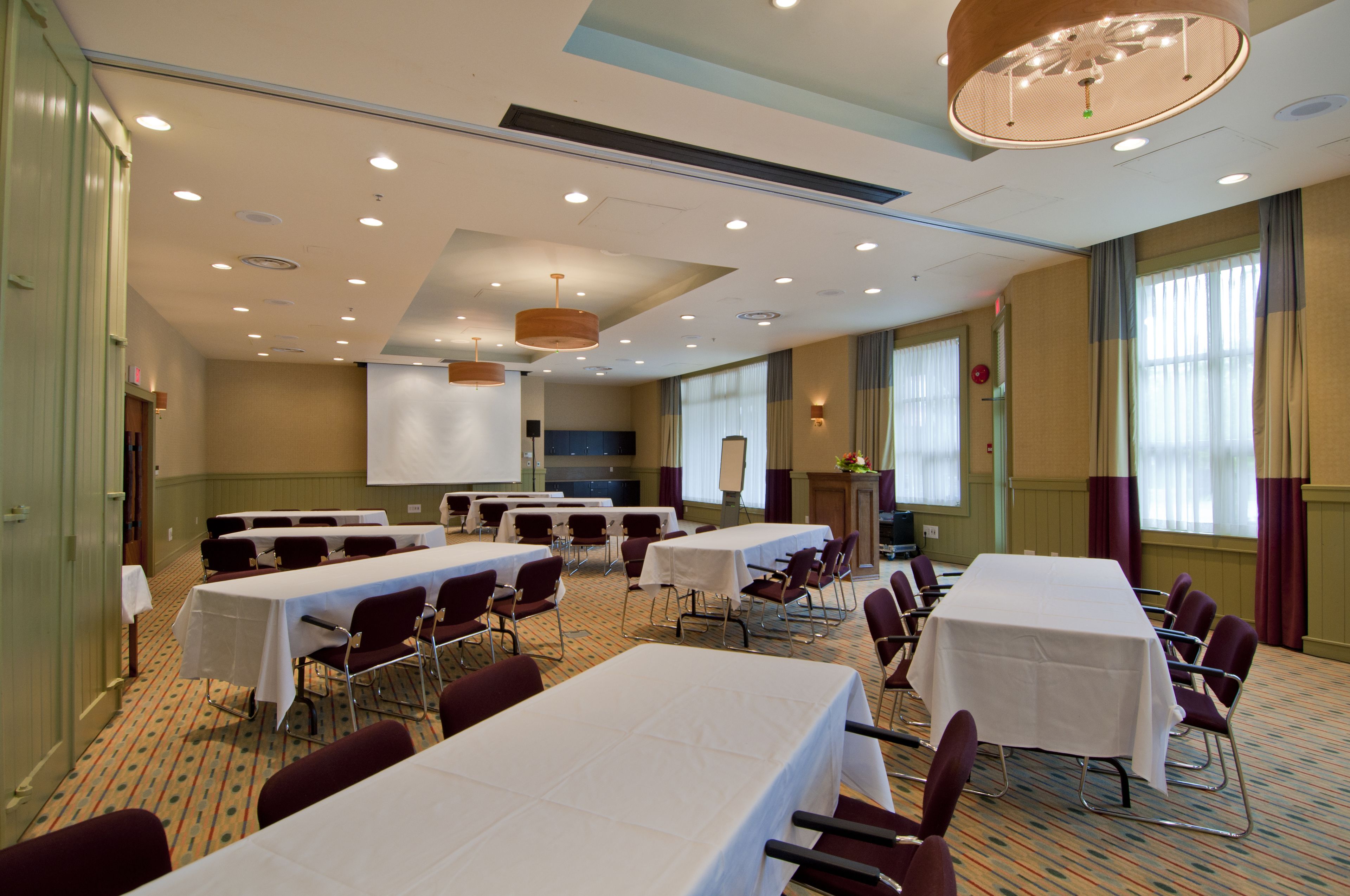 A conference room with multiple tables and chairs, equipped with a projector screen and a large chandelier.