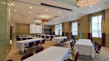 A conference room with multiple tables and chairs, equipped with a projector screen and a large chandelier.