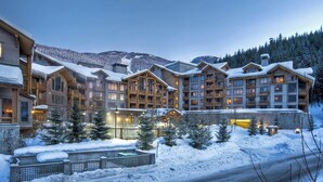 A multi-story lodge with wooden exteriors and balconies, surrounded by snow-covered trees and mountains. - First Tracks Lodge, by Lodging Ovations (Whistler)