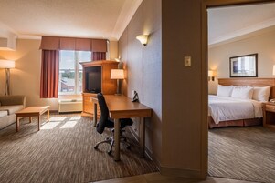 A hotel room with a bed, a desk with a chair, a TV, and a lamp.